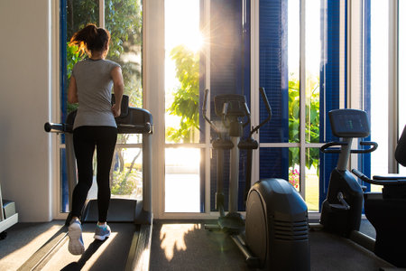 Good shape woman running on treadmill in indoor gym in morning light. Concept for healthcare of modern people.の写真素材