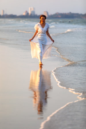 Woman wear white dress walking alone on sand beach and looking to camera, wet  in sea water with happiness manner.の写真素材