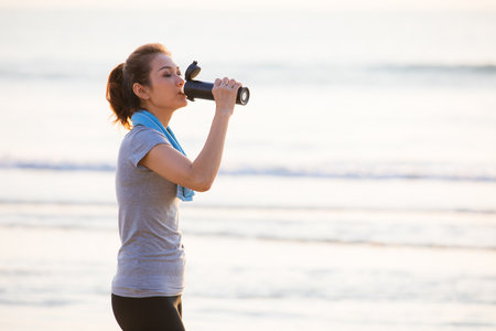 Woman holding bottle of clean water and drink in sunlight after exercise. Concept for health care and good lifestyle of modern people.の写真素材