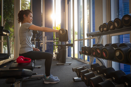 Asian woman exercise in fitness, lifting barbell for arms musculars in sunlight of morning.の写真素材