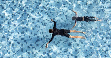 Two boys funny swimming together in clear water pool, taken from aerial view.の写真素材