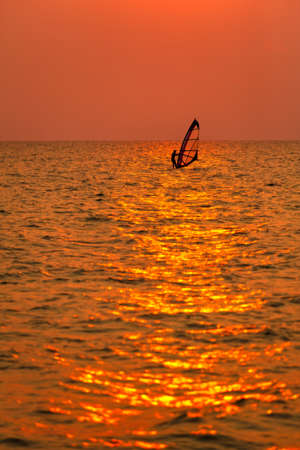 Surfer play windsurf alone in sea in twilight with wave in foreground and skyline in background.の写真素材