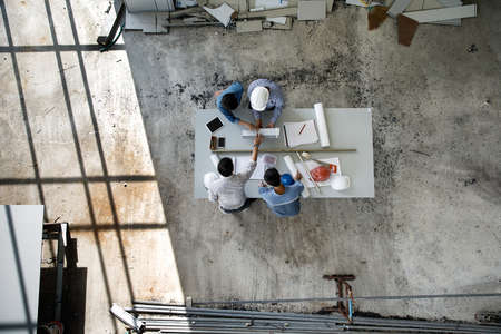 Four persons team of engineers talk together to review constuction material, taken from high angle, top view photoの写真素材