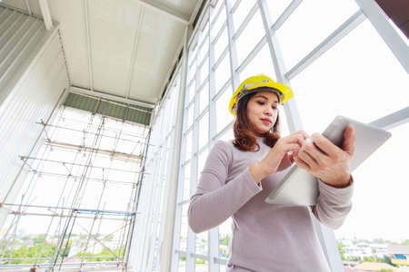 Female engineer in yellow safty helmet is looking to tablet computer while checking for under...