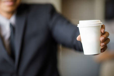 Businessman in black suit holding white paper coffee cupの写真素材