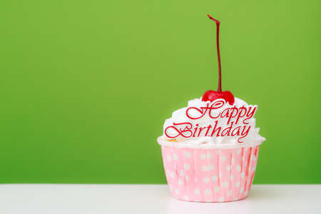 Beautiful cup cake with red cherry on top  and green backgroundの写真素材