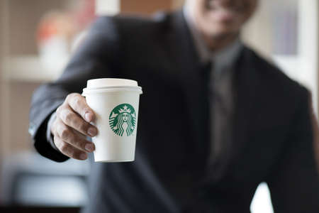 BANGKOK, THAILAND - JULY, 2 2017 : Businessman in suit holding Starbuck coffee cup in hand, Starbuck in the most popular premium coffee in Thailandのeditorial素材