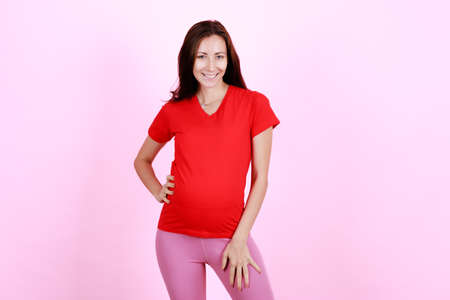 Half length portrait of beautiful caucasian young pregnant model shows her belly with smile face. Pregnant happy new mother posing indoor and looking with proud to camera. Love and family concept.の写真素材