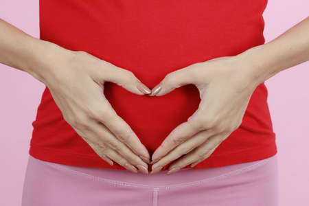 Hands of a mother putting on belly in heart sign or symbol. Concept of love, care and woman awaiting for coming newborn baby. Close-up shot.の写真素材