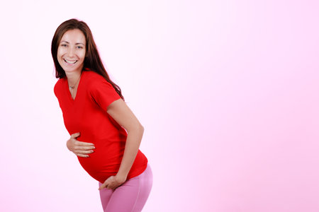Half length portrait of beautiful caucasian young pregnant model caressing tender touch her belly. Pregnant happy new mother posing indoor put hand soft touching on tummy. Love and family concept.の写真素材