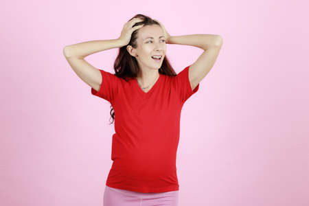 Young and beautiful pregnant woman in red t-shirt using hands holding her head with furious and stress gesture.の写真素材