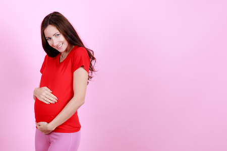 Half length portrait of beautiful caucasian young pregnant model caressing tender touch her belly. Pregnant happy new mother posing indoor put hand soft touching on tummy. Love and family concept.の写真素材