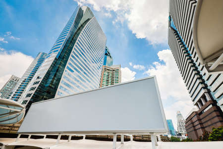 Blank white advertising billboard with modern city business center buildings in background with blue sky. Concept of advertising, advertisement, and mass marketing.の写真素材