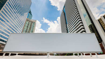 Blank white advertising billboard with modern city business center buildings in background with blue sky. Concept of advertising, advertisement, and mass marketing.の写真素材