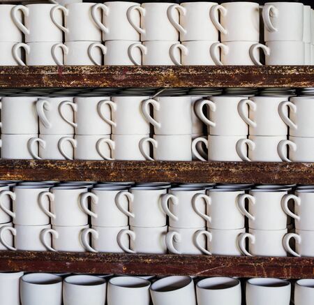 Stack of ceramic mugs in rackの写真素材