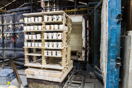 Ceramic mugs on racks in front of kiln in ceramic factory.のeditorial素材