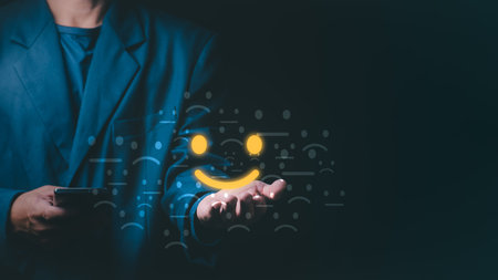 Businessman holding a glowing yellow smiley face icon representing customer satisfaction, positive feedback, and excellent service experience amidst various faded emotional emojis on dark backgroundの写真素材