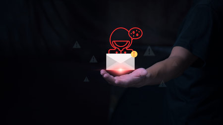 A hand holding a glowing envelope icon with a red hacker avatar and warning signs, representing...