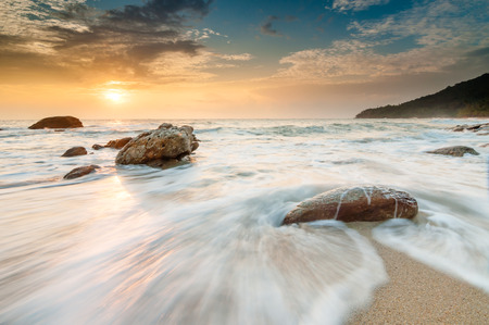 sea waves lash line impact rock on the beach at sunriseの写真素材