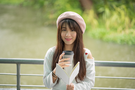 Portrait of young Asia woman reading a book and holding a hot cup of coffeeの写真素材
