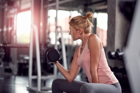 Strong woman working out with dumbbells, doing exercises in gymの写真素材