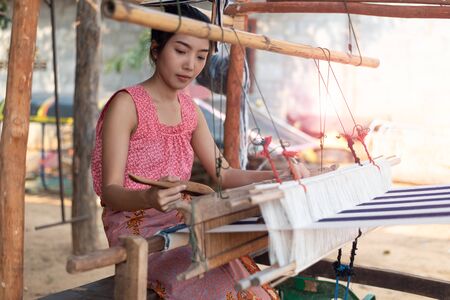 Young Asia women weaving with traditional Thai weaving machineの写真素材