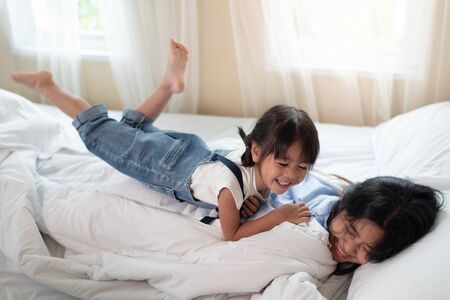Happy Asian family loving children, kid and her sister relaxing together in bed, love and happiness conceptの写真素材