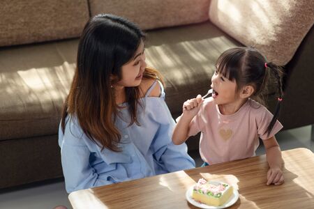 Happy Asian child enjoy eating tasty cake with her older sister, love and happiness family conceptの写真素材
