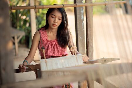 Young Asia women weaving with traditional Thai weaving machineの写真素材