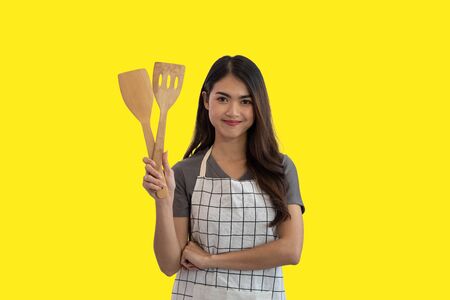 Young Asian woman cook holding a wooden spatula isolated on yellow studio