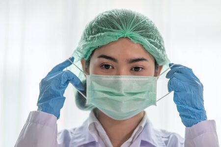 Coronavirus outbreak, Young Asian Female Doctor putting on a medical disposable mask to avoid...