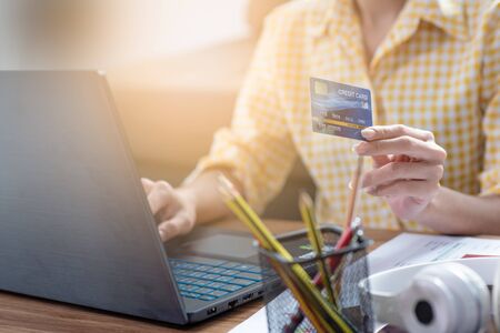 Close-up of woman holding credit card and using laptop for online shoppingの写真素材