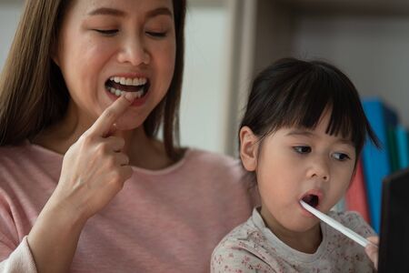 Asian mother teaching daughter to brush teeth in bathroomの写真素材