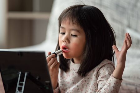 Asian little girl learning use cosmetic by themselves, she use lipstick paint on her lips, make up artistの写真素材