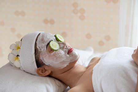 Beauty young Asian woman relax and lying on massage bed with fresh cucumber mask on eyes in spa...