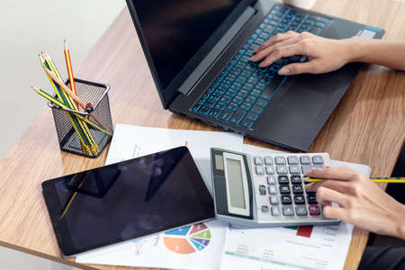 Close up of a businesswoman hands typing in a laptop and using calculator at her house, work from...