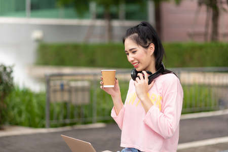Portrait of Young Asian woman enjoy listening to music with headphones and holding a hot cup of...
