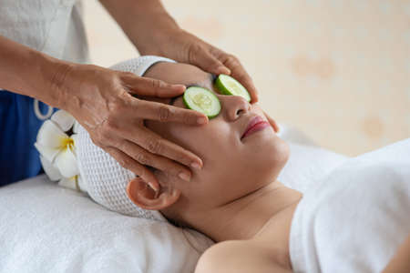 Beauty young Asian woman relax and lying on massage bed with fresh cucumber mask on eyes in spa salonの写真素材