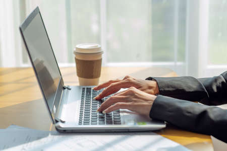 Close up of a businesswoman hands typing in a laptop in the office with cup of coffee, business conceptの写真素材