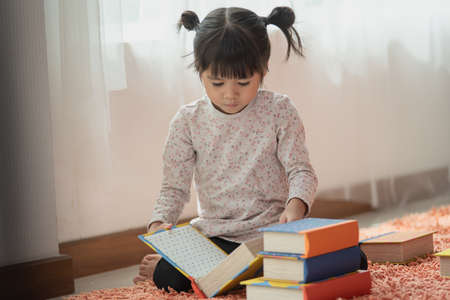 Happy Asian child little girl reading books in her house, education conceptの写真素材
