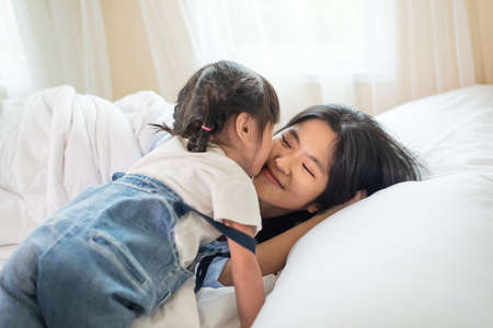 Happy Asian family loving children, kid and her sister kissing and relaxing together in bed, love and happiness conceptの写真素材