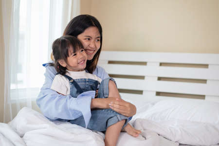 Happy Asian family loving children, older sister hugging her sister, relaxing together in bed, love and happiness conceptの写真素材