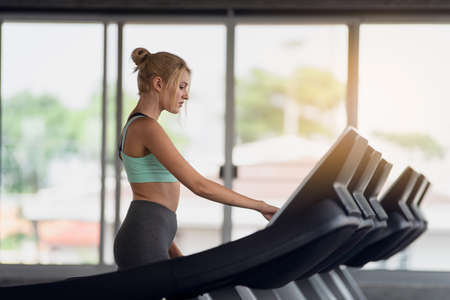 Attractive young sports woman is working out in gym, doing cardio training on treadmill, Running in...