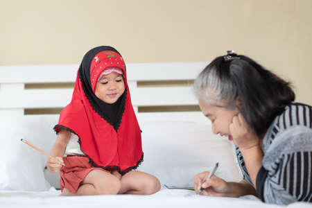 Young muslim girl writing a book with grandma, little islamic child do homework at homeの写真素材