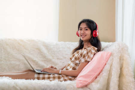 Portrait of Young Asian woman enjoy listening to music with headphones and using laptop, happy and...