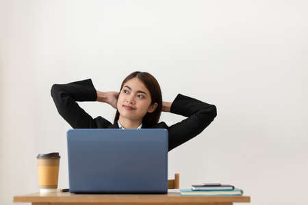 Portrait of Happy young Asian business woman relaxing with hands behind her head while working in...