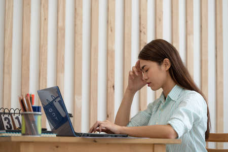 Stressed Asian business woman working on a laptop at her house, work from home, business concept