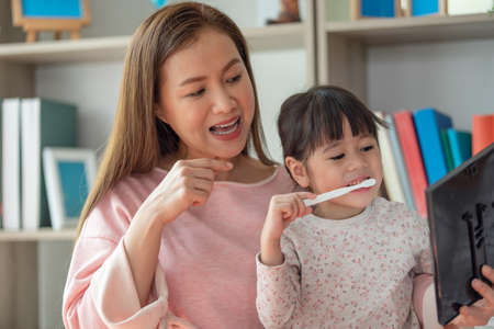 Asian mother teaching daughter to brush teeth in bathroomの写真素材