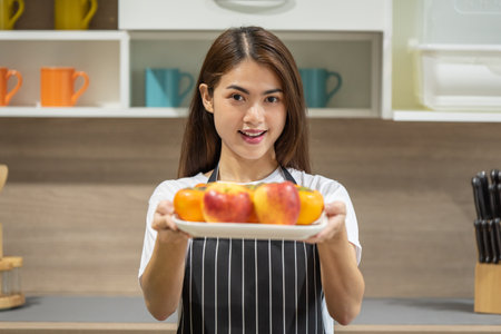 Portrait of happy young Asian woman holding fresh apple fruit in the modern kitchenの写真素材