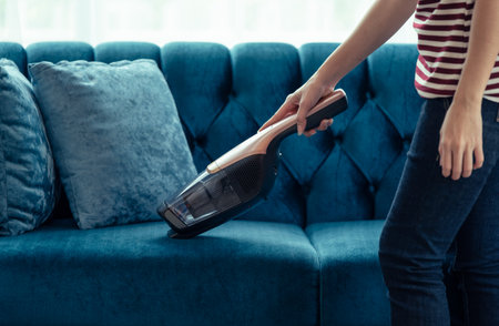 Close up of A woman housewife vacuuming furniture in a house with a hand-held portable vacuum cleanerの写真素材